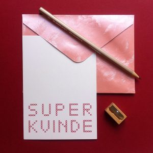 Setting with "Super Kvinde" postcard in pink with envelope, pencil, and pencil sharpener